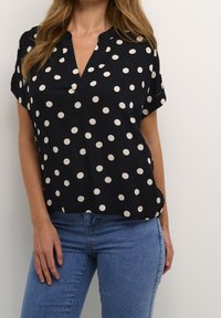 Marineblå kortærmet bluse med store hvide prikker, v-hals design og blød tekstur. Sammen med tætsiddende blå jeans for kontrast.