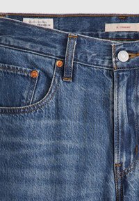 Mörkblå denimjeans med rak skärning, prydda med kopparfärgad hårdvara, kontrasterande sömmar och en mjuk, texturerad yta.