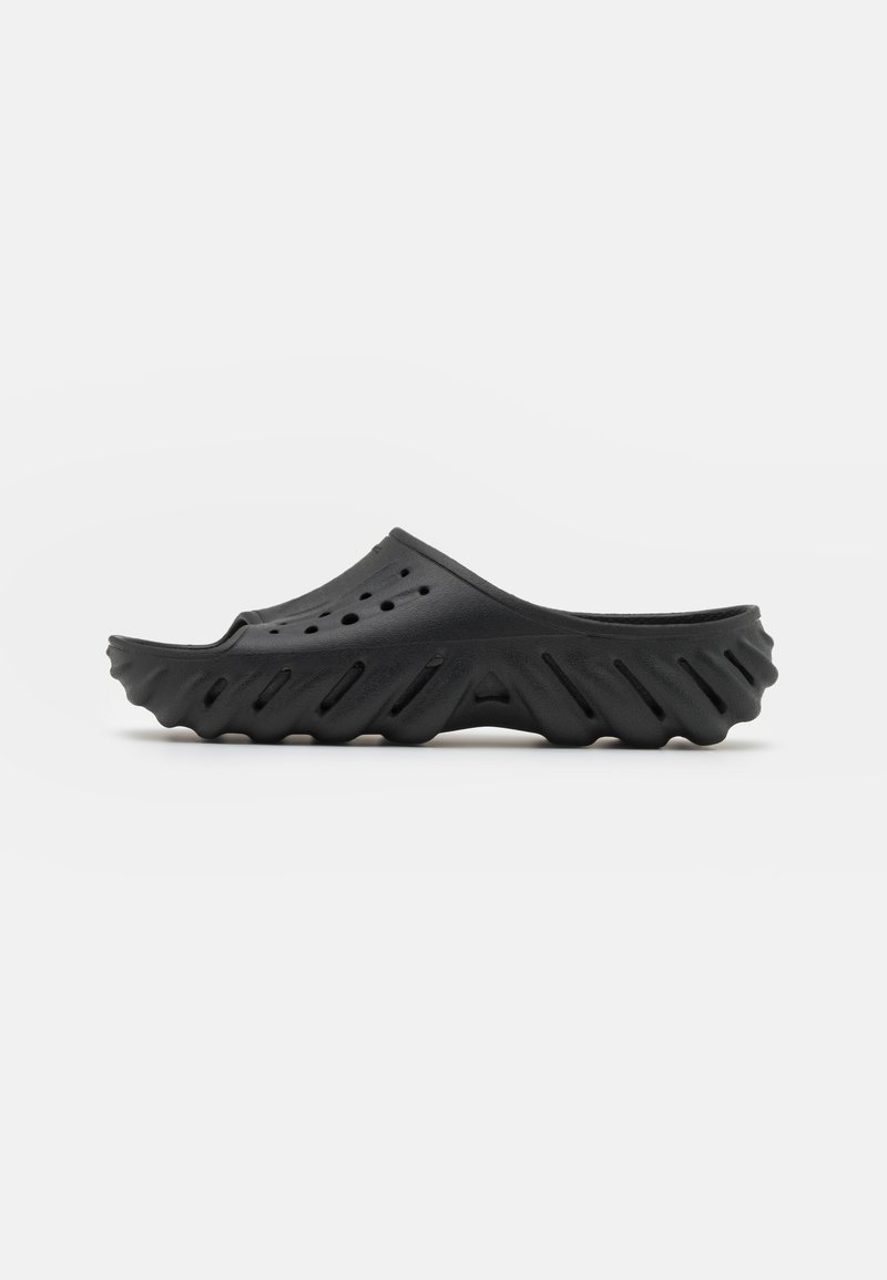 Crni slip-on klompe od gume, s teksturiranom petom koja ima valoviti dizajn, ventilacijskim rupama na gornjem dijelu i niskim, zaobljenim profilom.