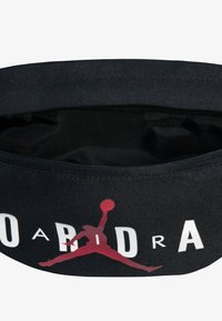 Pochete preta com fecho zip e logótipo Jumpman vermelho, acompanhado de texto branco. A textura parece suave, com um design de tecido durável.