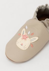 Beige lærslipper med en brodert kaninansikt. Har en scalloped kant og dekorative blomstelementer i rosa og blå.