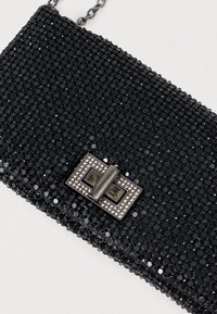 Černá kabelka na ruku pokrytá flitry s obdélníkovým kovovým zapínáním s průhlednými a tmavými akcenty, připevněný řetízek.