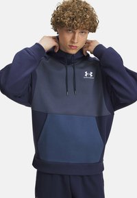Marineblå hoodie med et to-farvet design, der har en lysegrå frontpanel, snøre i hætten og en frontlomme. Under Armour-logoet vises.