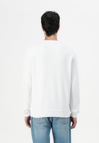 Sudadera blanca de tejido suave, con mangas largas y escote redondo, combinada con jeans de un azul claro. Diseño minimalista.