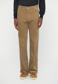 Brūnas korduroja bikses ar taisnu kāju dizainu, kurām ir priekšējās kabatas un pogu aizdare jostas daļā. Apvienotas ar brūniem sporta apaviem.