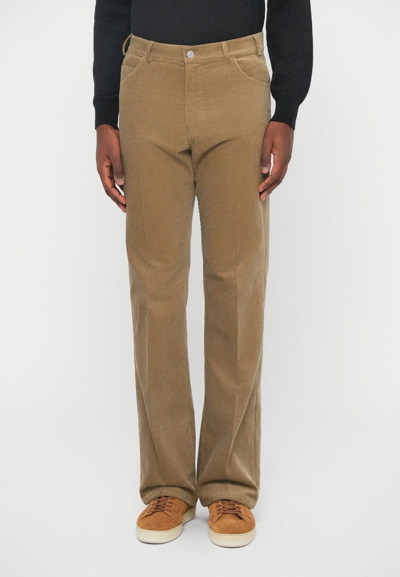 Brune babyfløjsbukser med lige ben, synlige syninger, forlommer og knaplukning. Båret med brune sneakers.