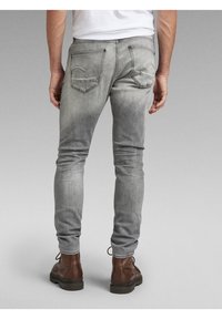 Jeans de denim gris ajustados con un efecto desgastado, que cuentan con dos bolsillos traseros, detalles de costura y se combinan con botas de cuero marrón.