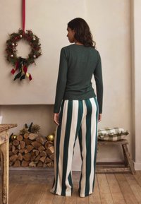 Long-sleeve, dark green top with a crew neckline, paired with wide-leg trousers featuring vertical green and white stripes. Wool wreath in background.