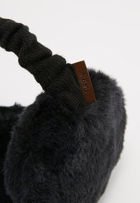 Orejeras de pelo sintético negro con una banda de punto negra, que presenta una etiqueta de cuero marrón grabada con "Barts". Textura suave para mantener el calor.