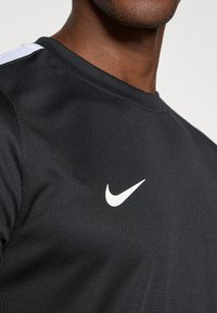 Μαύρο αθλητικό μπλουζάκι Nike με υφή, στρογγυλή λαιμόκοψη και λευκό λογότυπο στην αριστερή πλευρά του στήθους. Λευκή λεπτομέρεια στον ώμο.