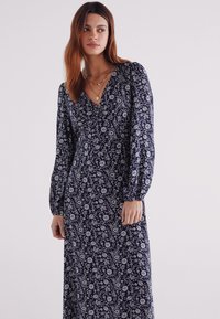Das navyfarbene Kleid mit Blumenmuster besitzt einen V-Ausschnitt, lange Puffärmel und ein fließendes Design, das aus leichtem Stoff gefertigt ist.