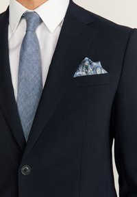Costume bleu marine avec une chemise blanche et une cravate texturée bleue. Le mouchoir de poche présente un motif paisley bleu et blanc. Bouton à l'avant.