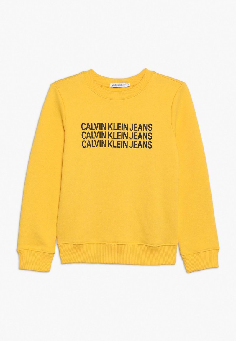 Sudadera amarilla con texto negro "CALVIN KLEIN JEANS" repetido varias veces. Hecha de tela suave con cuello redondo y puños acanalados.
