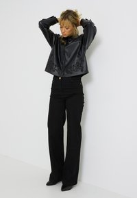 Veste noire en simili cuir cropped avec broderies florales, assortie à un pantalon taille haute noir et des talons aiguilles noirs.