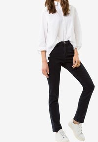 Valkoinen napillinen paita, mustat slim-fit farkut, valkoiset tennarit. Pehmeä kangas, yksinkertainen muotoilu ja normaali pituus. Ei näkyviä kuvioita tai koristeita.