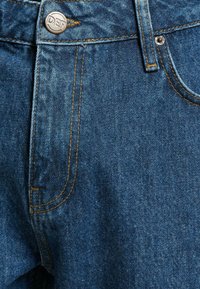 Blauwe denim jeans met een ritssluiting, knoopsluiting met "DEF" gravure en contrasterende oranje stiksels op de zakken en naden.