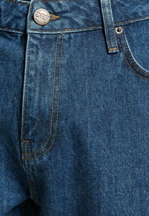 Jean en denim bleu avec une fermeture éclair, un bouton avec gravure "DEF" et des coutures oranges contrastantes sur les poches et les coutures.