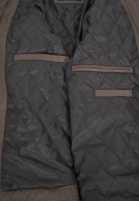 Quilted inner lining of a jacket, gray with diagonal pattern, featuring two flat pockets and one zippered pocket, finished with beige accents.