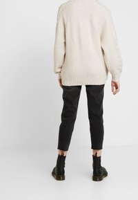 Beige pletený svetr s texturovaným povrchem a žebrovaným lemem, v kombinaci s úzkými černými kalhotami a černými kotníkovými botami.