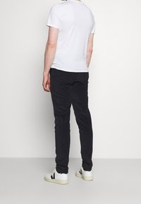 Bílá tričko s krátkým rukávem nošené s tmavými slim-fit kalhotami a bílými teniskami. Tkanina vypadá jemně; outfit má ležérní design.