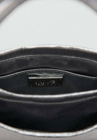 Black leather handbag interior with silver accents. Features a branded tag, smooth texture, and two compartments for organization.