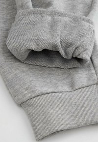 Szary materiał bluzy z ribbowanym mankietem, ukazujący gładką fakturę i złożony rękaw. Materiał wydaje się miękki i swobodny.