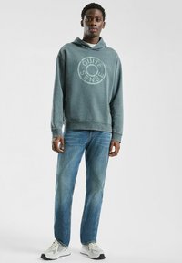 Szary sweatshirt z kapturem z okrągłym napisem "Quite Sense"; noszony z jasnoniebieskimi dżinsami i białymi trampkami z szarymi akcentami.