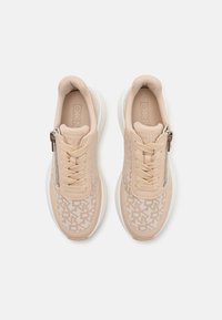 Beige atletiske sko med teksturert stoff, logo-mønster, kremfargede snørebånd og glidelås på siden. Tykk hvit såle med avrundede kanter.