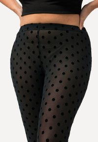 Schwarze durchsichtige Leggings mit schwarzen Samt-Punkten, ausgestattet mit einem glatten Bund und einem taillierten Design, das die Beine betont.