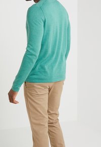 Teal långärmad skjorta i texturerat tyg, parat med beige byxor. Skjortan har rund halsringning och åtsittande ärmar.