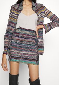 Conjunto de camisa y falda con un patrón de zigzag multicolor en una tela texturizada. La camisa tiene un cuello y mangas largas; la falda es ajustada.