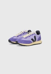 Purple sneakers with suede and mesh materials, light yellow sole, black accents, and beige laces, featuring a logo on the tongue.