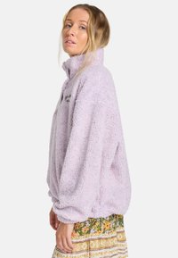 Fuzzy lila fleece pullover met hoge kraag en een relaxte pasvorm. Voorzien van geborduurd logo op de borst en elastische boorden.