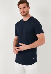 Navy plava, majica kratkih rukava od pamuka. Okrugli izrez s ravnim rubom. Mala oznaka s logotipom na donjoj strani. Glatka tekstura.