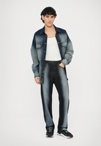 Jeans srajca z modrim prelivnim odtenkom, dolgi rokavi, zapenjanje na gumbe, kombinirana s temno modrimi jeans hlačami in črnimi športnimi čevlji.