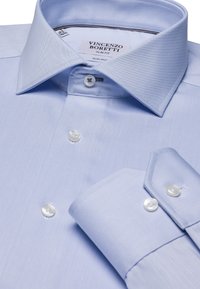 Lichtblauw, slim fit overhemden. Kenmerken een puntkraag, gladde textuur, en vier witte knopen met een subtiel diagonaal ribbelpatroon.