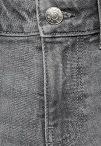 Grå denimtyg med en närbild av en knappstängning och sömdetaljer. Texturen är slät med ett subtilt vävmönster.