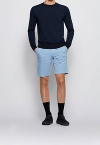 Suéter navy, pantalones cortos azul claro y zapatos negros con calcetines negros. El material del suéter parece ser de punto, mientras que el de los pantalones cortos parece ser tejido.