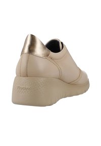 Zapatilla de cuero beige con un acento metálico dorado en el talón, suela texturizada y diseño liso. Nombre de la marca "Fluchos" estampado en el lateral.