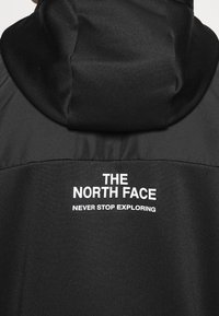Czarna kurtka z kapturem z logo "THE NORTH FACE" oraz napisem "NEVER STOP EXPLORING" w białym tekście na plecach.