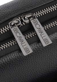 Black textured leather accessory with two metallic zippers featuring engraved branding. Close-up shows detailed stitching and zipper teeth.