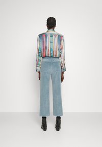 Gestreifte mehrfarbige Bluse mit Knopfverschluss, kombiniert mit hellblauen Cord-weitbeinigen Hosen und schwarzen Knöchelstiefeln.