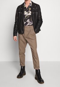 Czarna skórzana kurtka z srebrnymi suwakami, wzorzysta koszula z krótkim rękawem, beżowe spodnie i czarne sznurowane buty na grubej podeszwie.