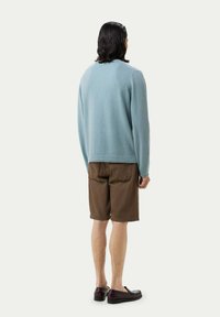 Helles blaues Sweatshirt mit Rundhalsausschnitt, getragen über braunen Shorts. Der Stoff wirkt weich, und die Schuhe sind dunkel und haben ein elegantes Design.