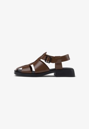 Brun læder sandal med åben tå, sort spænde rem og lav sort chunky hæl på hvid baggrund.