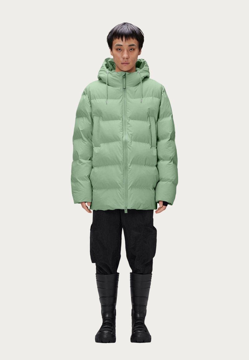 Veste courte, vert menthe, avec capuche, fermeture éclair à l'avant et cordons de serrage. Portée sur un pantalon cargo noir et des bottes noires hautes. Design simple.