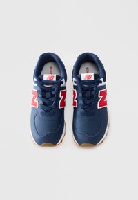 Une paire de baskets New Balance bleu marine avec des logos "N" rouges, des accents blancs et des semelles couleur gomme, vue du dessus sur un fond blanc.