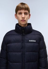 Marineblå dunjakke med høj krave, lynlås lukning og broderet logo. Stoffet er glat med et quiltet design og varm isolering.