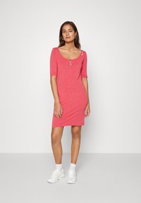 Vestido vermelho ajustado com mangas curtas, decote redondo e detalhe de botões. Apresenta um pequeno padrão de bolinhas brancas. Combinado com ténis brancos.
