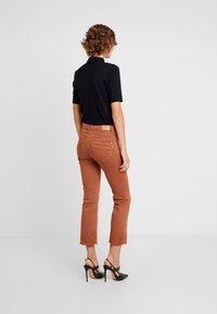 Pantalons courts de couleur rouille avec une bordure en dentelle à l'ourlet, associés à un haut noir à manches courtes. Des chaussures à talons hauts noires complètent la tenue.